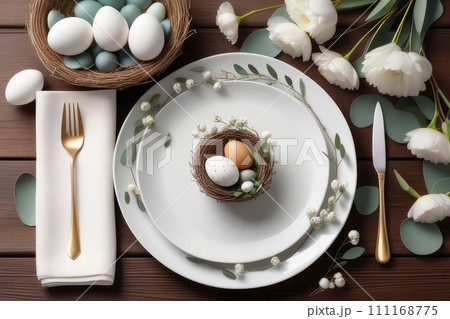 Table with served plates, napkin, cutlery, easter eggs in a bird's nest and eucalyptus branch. 111168775