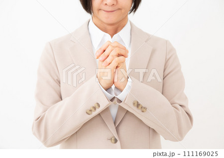 手を合わせてお願い事をするベージュのスーツを着たミドル女性 111169025