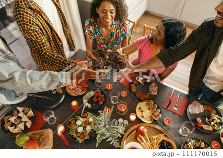 Group of happy friends is drinking wine and clinking glasses having holiday dinner party at home 111170015