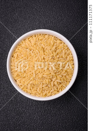 Raw risoni pasta made from durum wheat on a dark concrete background Raw risoni pasta made from durum wheat on a dark concrete background 111171375