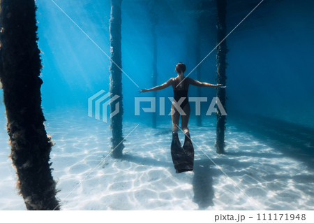 Woman freediver with fins posing under the pier in clear ocean. Female swims with fins under the pier 111171948