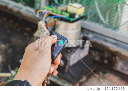 Man hand pressing remote control to open gate door. 111172146