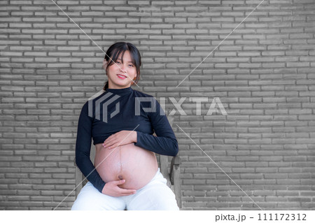 Mom pregnant woman in a dress holds hands on belly on black brick background, Waiting for the birth of your baby with love Mom pregnant woman in a dress holds hands on belly on black brick background, Waiting for the birth of your baby with love 111172312