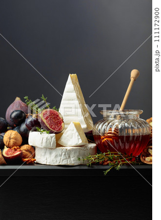 Camembert cheese with fruits and honey on a black background. Camembert cheese with fruits and honey on a black background. 111172900