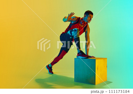 Athlete in sportswear training, doing exercises with wooden box against gradient blue yellow background in neon light Athlete in sportswear training, doing exercises with wooden box against gradient blue yellow background in neon light 111173184