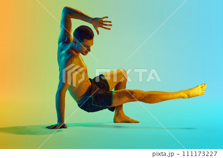 Young shirtless man with muscular, relief, strong body training, doing workout exercises against gradient blue yellow background in neon light Young shirtless man with muscular, relief, strong body training, doing workout exercises against gradient blue yellow background in neon light 111173227