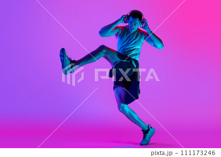 Young muscular man in sportswear, wearing headphones and training against gradient pink background in neon light Young muscular man in sportswear, wearing headphones and training against gradient pink background in neon light 111173246