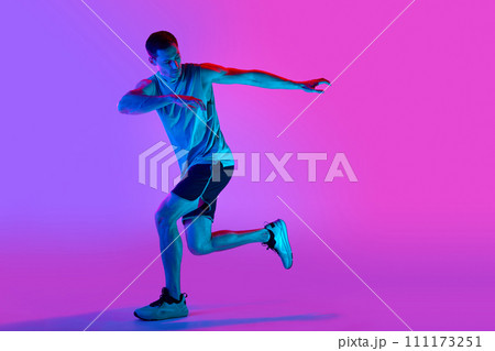 Warming-up exercises. Sportive young man in sportswear training, doing exercises against gradient pink background in neon light Warming-up exercises. Sportive young man in sportswear training, doing exercises against gradient pink background in neon light 111173251