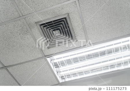 Ceiling mounted cassette type air conditioner and modern lamp light on white ceiling. Duct air conditioner for home, hall or office. Ceiling mounted cassette type air conditioner and modern lamp light on white ceiling. Duct air conditioner for home, hall or office. 111175273