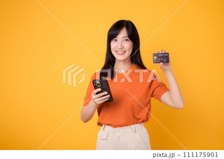 Dynamic young Asian woman in her 30s, using smartphone and holding credit card on yellow background. Secure online payment. 111175901