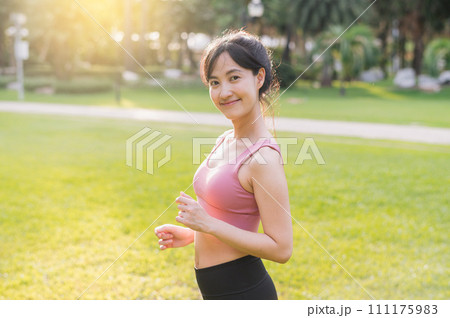 Experience the joy of wellness living as a happy, beautiful 30s Asian woman smiles and looks at the camera in a park at sunset. 111175983