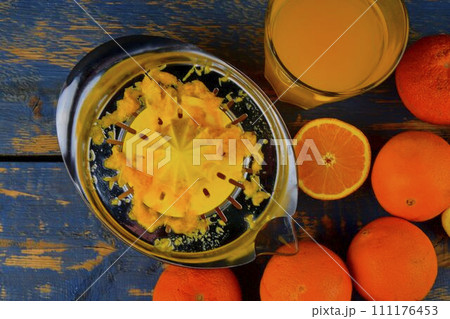 Tangerines, oranges, a glass of orange juice and manual citrus squezeer on blue wooden background. Oranges cut in half. Top view, flat design Tangerines, oranges, a glass of orange juice and manual citrus squezeer on blue wooden background. Oranges cut in half. Top view, flat design 111176453