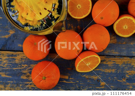 Tangerines, oranges, a glass of orange juice and manual citrus squezeer on blue wooden background. Oranges cut in half. Top view, flat design 111176454