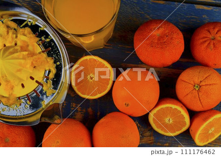 Tangerines, oranges, a glass of orange juice and manual citrus squezeer on blue wooden background. Oranges cut in half. Top view, flat design Tangerines, oranges, a glass of orange juice and manual citrus squezeer on blue wooden background. Oranges cut in half. Top view, flat design 111176462