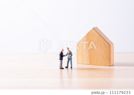 木製の住宅模型の前で握手するミニチュアビジネスマン 111179233