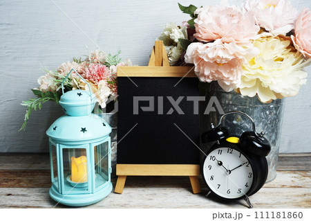Easel mockup with blue landtern, alarm clock and flowers bouquet decoration on wooden background Easel mockup with blue landtern, alarm clock and flowers bouquet decoration on wooden background 111181860