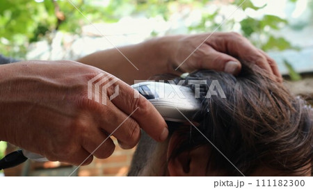 hands of a hairdresser cutting the back of a person's head with a clipper, close-up, shaving long dark hair from the back and top of the head with a trimmer with an attachment hands of a hairdresser cutting the back of a person's head with a clipper, close-up, shaving long dark hair from the back and top of the head with a trimmer with an attachment 111182300