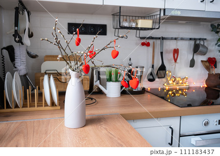 The interior of the kitchen in the house is decorated with red hearts for Valentine's Day. Decor on the table, stove, utensils, festive mood in a family nest 111183437