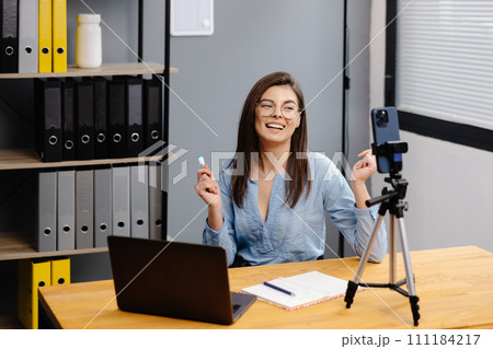 Videoconference And Training. Class of diverse students learning remotely online using web app. Female teacher providing lesson with laptop, recording video on cellphone on tripod Videoconference And Training. Class of diverse students learning remotely online using web app. Female teacher providing lesson with laptop, recording video on cellphone on tripod 111184217