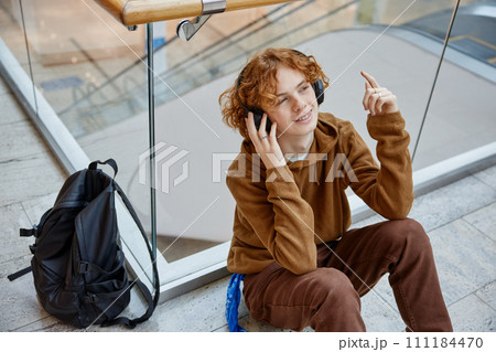 Teenager boy relaxing at shopping mall sitting on floor listening music 111184470