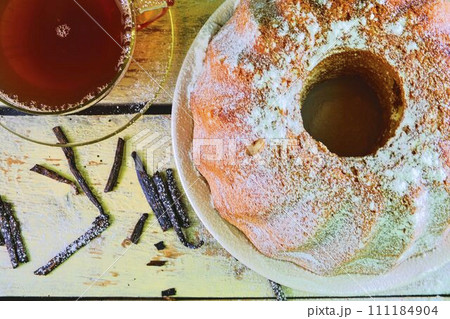 Old fashioned sand cake with cup of black tea and pieces of vanilla on wooden background. Egg-yolk sponge cake on rustic white background. Top view. Flat design 111184904