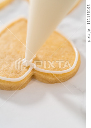 Decorating heart-shaped sugar cookies with pink and white royal icing for Valentine's Day. Decorating heart-shaped sugar cookies with pink and white royal icing for Valentine's Day. 111186198