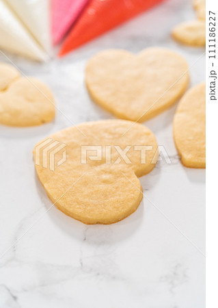Decorating heart-shaped sugar cookies with pink and white royal icing for Valentine's Day. Decorating heart-shaped sugar cookies with pink and white royal icing for Valentine's Day. 111186227