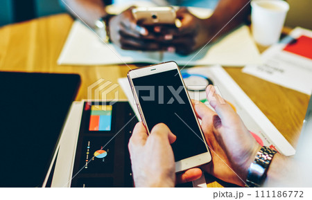 Multiracial pensive persons browsing smartphone at round table in office Multiracial pensive persons browsing smartphone at round table in office 111186772
