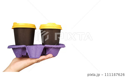 Female hand holding and serving two disposable cups of coffee on a white background with copy space in the studio. Breakfast on the go. Paper glasses with hot drinks in black and yellow plastic lids Female hand holding and serving two disposable cups of coffee on a white background with copy space in the studio. Breakfast on the go. Paper glasses with hot drinks in black and yellow plastic lids 111187626