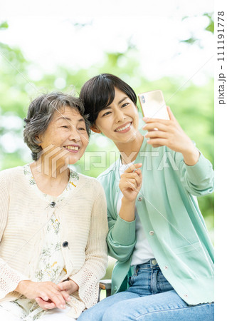 スマートフォンで自撮りするシニア女性と若い女性 111191778