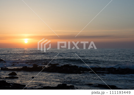 水平線に沈む夕陽と岩の海岸 111193449