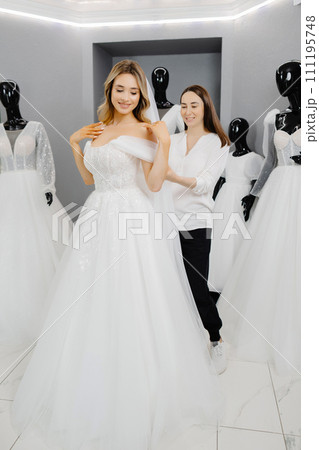 The bride-to-be chooses a dress for the wedding. A dressmaker's assistant is fitting a dress for the bride The bride-to-be chooses a dress for the wedding. A dressmaker's assistant is fitting a dress for the bride 111195748