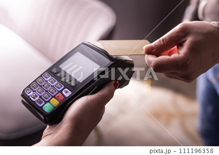 NFC credit card payment. Woman paying with contactless credit card with NFC technology. Wireless money transaction. Card machine in male hand on sunlight background NFC credit card payment. Woman paying with contactless credit card with NFC technology. Wireless money transaction. Card machine in male hand on sunlight background 111196358