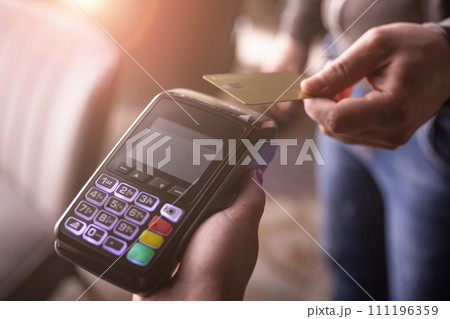 NFC credit card payment. Woman paying with contactless credit card with NFC technology. Wireless money transaction. Card machine in male hand on sunlight background 111196359