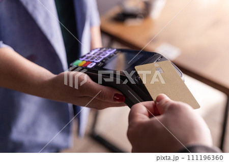 NFC credit card payment. Woman paying with contactless credit card with NFC technology. Wireless money transaction. Card machine in male hand on sunlight background 111196360