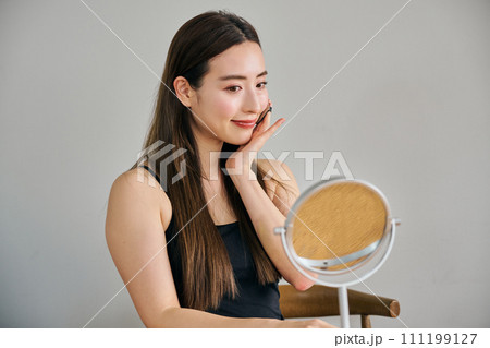 ファンデーションを塗るロングヘアの30代女性 111199127