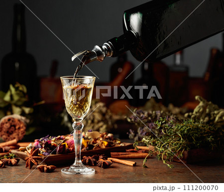 Yellow herbal liquor or mixture is poured from a vintage bottle into a glass. Yellow herbal liquor or mixture is poured from a vintage bottle into a glass. 111200070