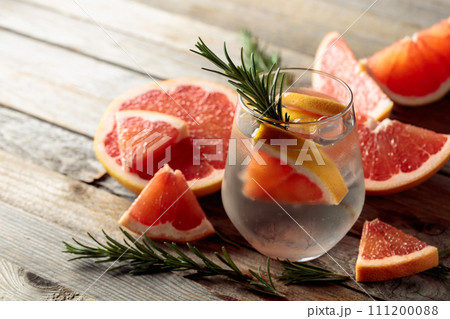 Gin tonic with ice, rosemary, and grapefruit slices on an old wooden table. Gin tonic with ice, rosemary, and grapefruit slices on an old wooden table. 111200088