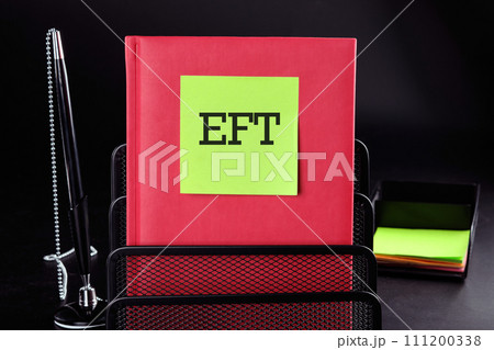 EFT Text on a yellow sticker on a red vertical notepad on a black background next to a pen and money EFT Text on a yellow sticker on a red vertical notepad on a black background next to a pen and money 111200338