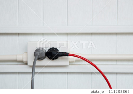 An electric plug with a gray and red cable in the socket. An electric plug with a gray and red cable in the socket. 111202865