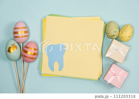 Greeting card for dentistry happy easter, space for text in center, tooth with painted eggs and gifts top view 111203318