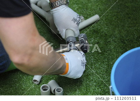 Plumber hands in gloves joining plastic pipes with the soldering iron for PVC pipes 111203511