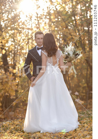 beautiful bride in white wedding dress and groom standing outdoor on natural background in sunny day 111203746