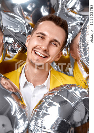 portrait of happy man in yellow jacket with a lot of silver air balloons. birthday party 111203768