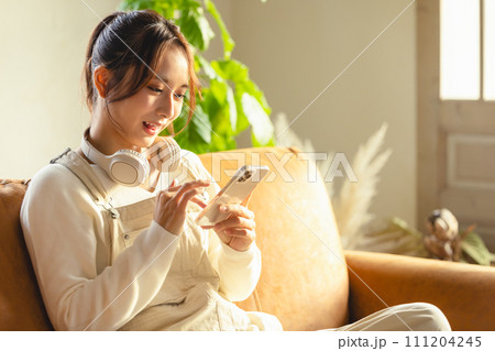 ソファーでスマホを使う女性 111204245