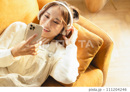 ソファで寝転んでスマホを使う女性 ソファで寝転んでスマホを使う女性 111204246