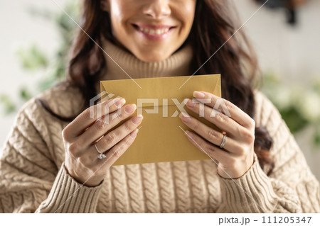 A smiling young woman holds a mail envelope made of recycled paper in her hands 111205347