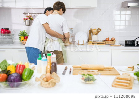 Young lgbtq Asian gay boyfriend hug partner in kitchen during cook 111208098