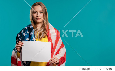 American woman with white a4 paper poster. Copy space. Smiling lady, blue studio American woman with white a4 paper poster. Copy space. Smiling lady, blue studio 111211546