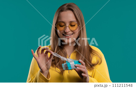 Happy woman gift box on blue background. Girl smiling, interested what's inside. Happy woman gift box on blue background. Girl smiling, interested what's inside. 111211548